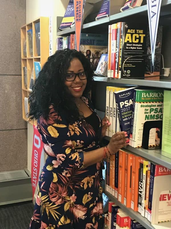 A woman posing in a bookstore aisle surrounded by books.